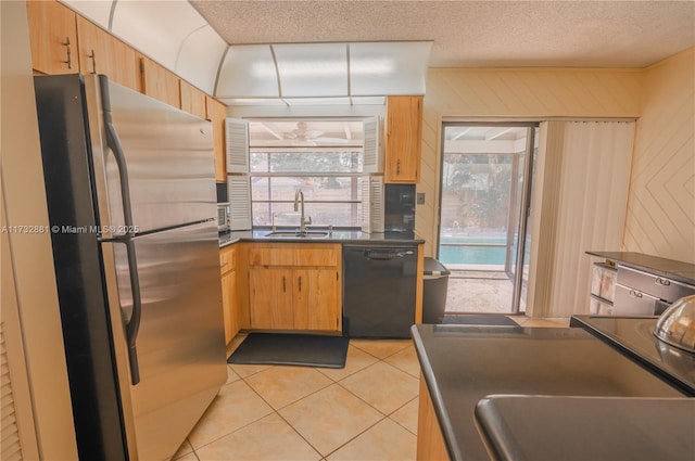 kitchen with light tile patterned floors, a sink, black dishwasher, freestanding refrigerator, and dark countertops