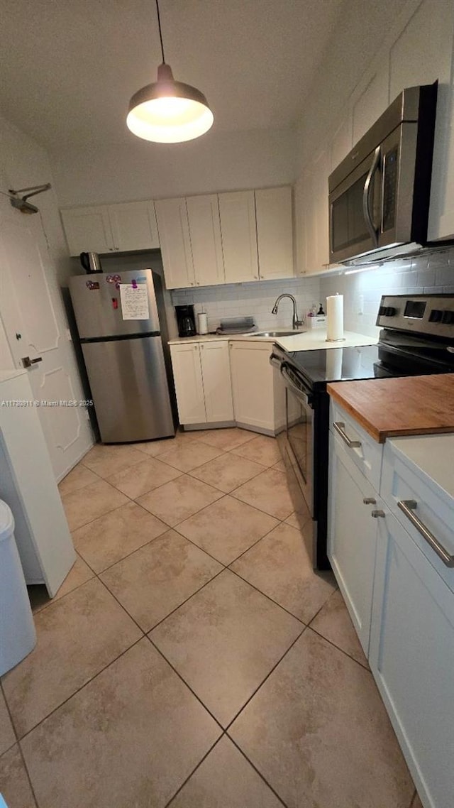 kitchen featuring pendant lighting, stainless steel appliances, white cabinets, and light tile patterned flooring