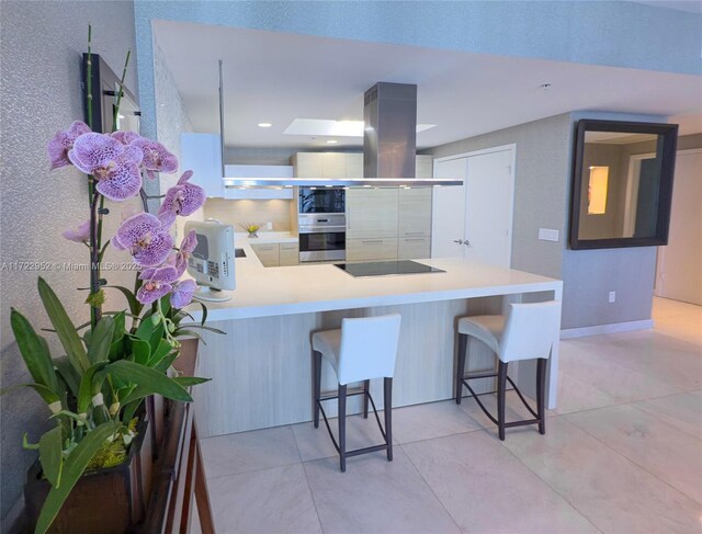 kitchen featuring a kitchen breakfast bar, island exhaust hood, black appliances, light tile patterned flooring, and kitchen peninsula