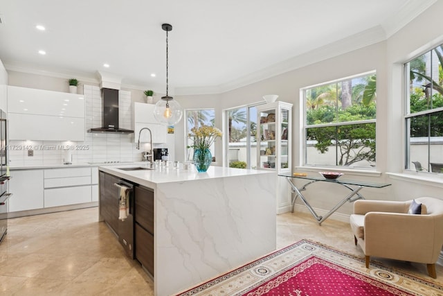 kitchen featuring wall chimney range hood, modern cabinets, a sink, and white cabinets