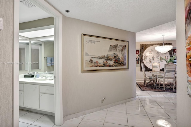 hall featuring light tile patterned flooring, sink, an inviting chandelier, and a textured ceiling