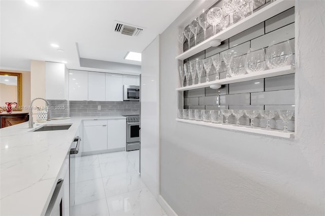 kitchen with sink, white cabinetry, tasteful backsplash, light stone counters, and appliances with stainless steel finishes