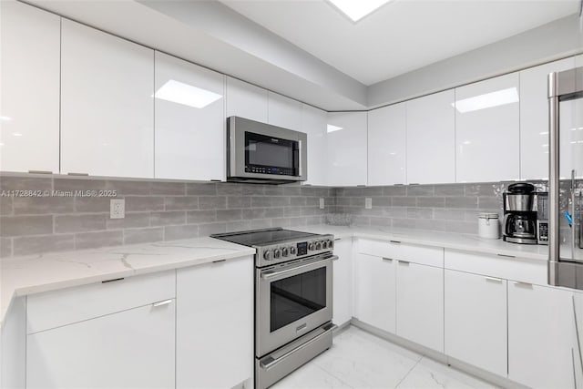 kitchen with tasteful backsplash, appliances with stainless steel finishes, light stone counters, and white cabinets