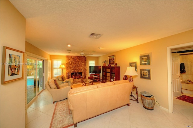 tiled living room with ceiling fan, a textured ceiling, and a fireplace