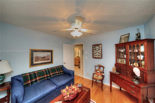 living room with ceiling fan, a textured ceiling, and light wood-type flooring