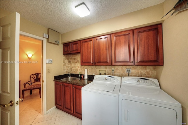 clothes washing area with sink, light tile patterned floors, cabinets, a textured ceiling, and washing machine and clothes dryer