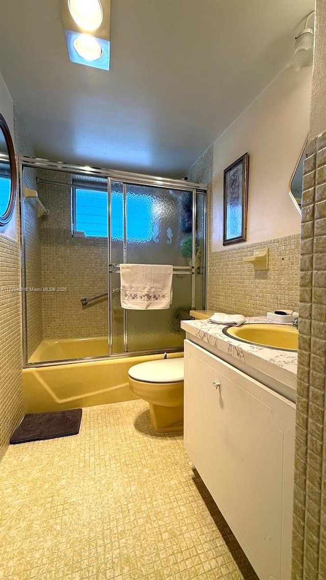 full bathroom with tile walls, vanity, toilet, and combined bath / shower with glass door