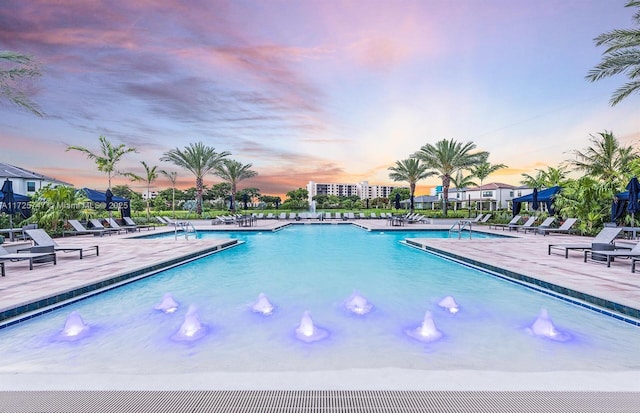 pool at dusk with pool water feature and a patio