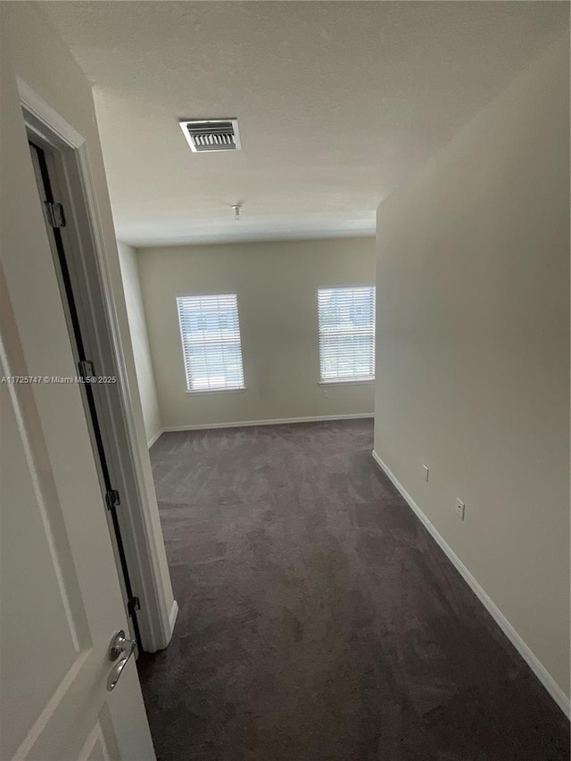 unfurnished room featuring baseboards, visible vents, and dark colored carpet