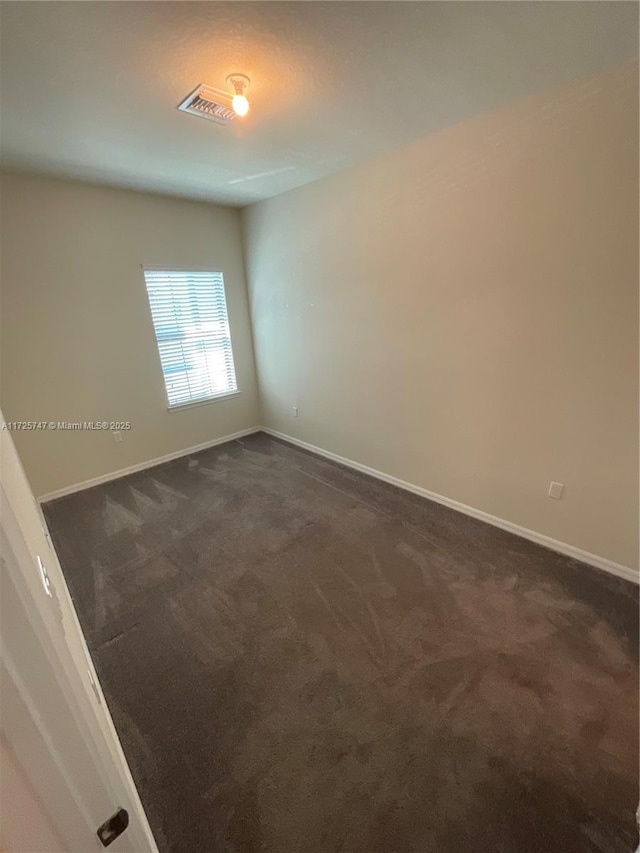 spare room featuring visible vents, baseboards, and dark colored carpet