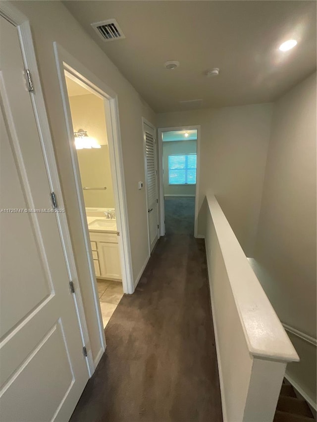 corridor featuring baseboards, visible vents, a sink, an upstairs landing, and dark carpet