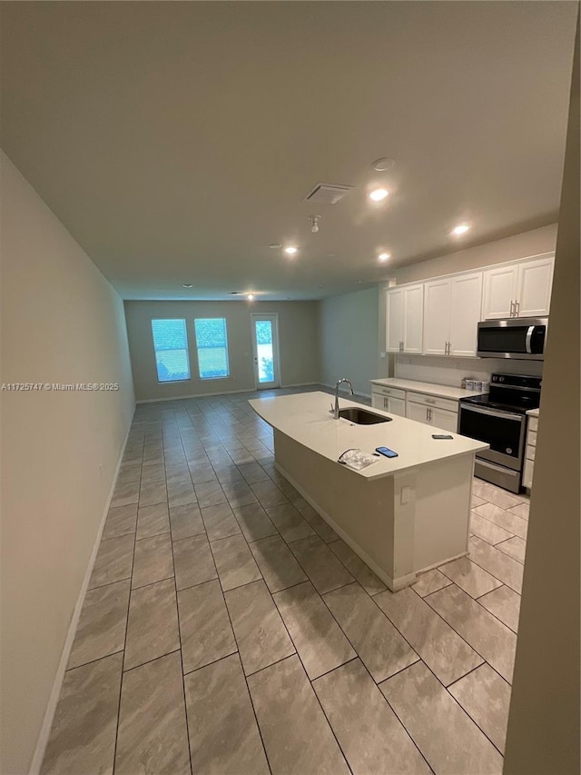 kitchen featuring a center island with sink, light countertops, appliances with stainless steel finishes, white cabinetry, and a sink