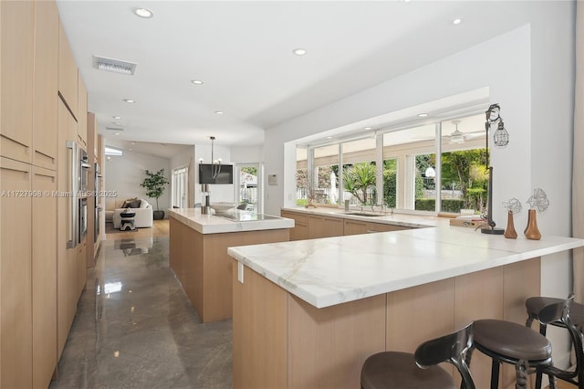 kitchen with light brown cabinetry, a breakfast bar, sink, a center island, and kitchen peninsula