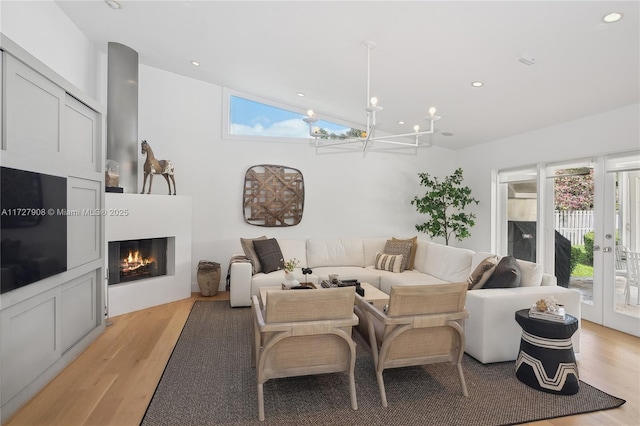 living room with vaulted ceiling, a notable chandelier, light wood-type flooring, and french doors