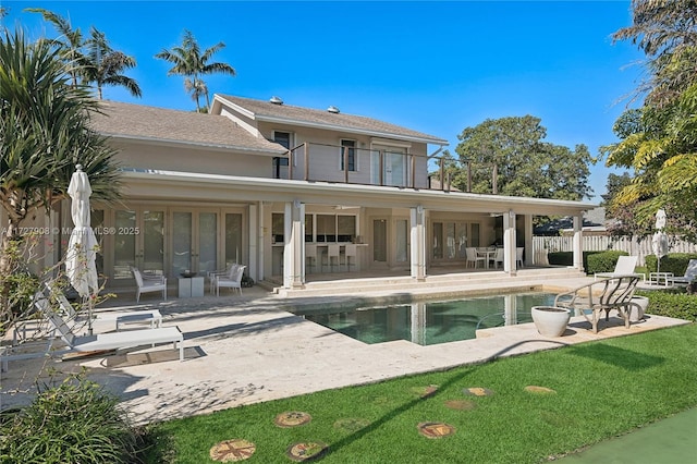 rear view of property featuring a fenced in pool, a balcony, and a patio area