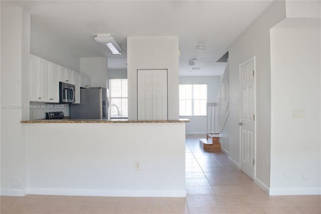 kitchen featuring white cabinets, light tile patterned floors, kitchen peninsula, stainless steel appliances, and light stone countertops