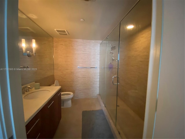 bathroom featuring tile walls, visible vents, toilet, a shower stall, and vanity