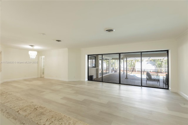 empty room with crown molding, a chandelier, and light hardwood / wood-style flooring