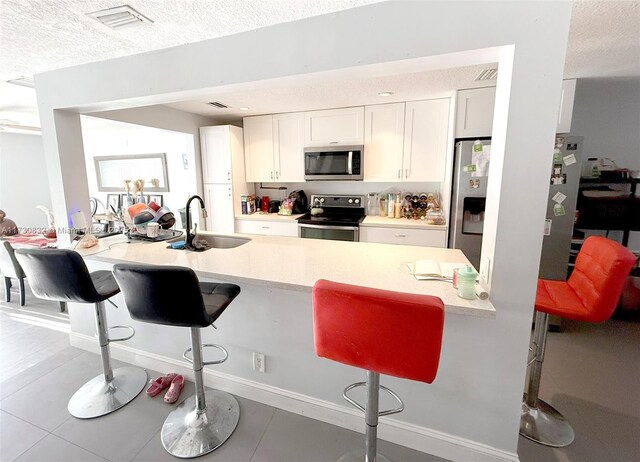 kitchen featuring a kitchen bar, sink, white cabinetry, light tile patterned floors, and stainless steel appliances