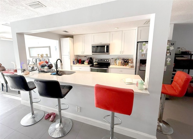 kitchen featuring sink, a breakfast bar, appliances with stainless steel finishes, white cabinetry, and a textured ceiling