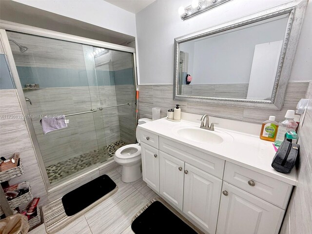 bathroom with a shower with shower door, tile walls, tile patterned flooring, vanity, and toilet