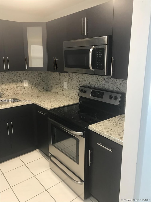 kitchen with sink, light tile patterned floors, stainless steel appliances, light stone countertops, and decorative backsplash