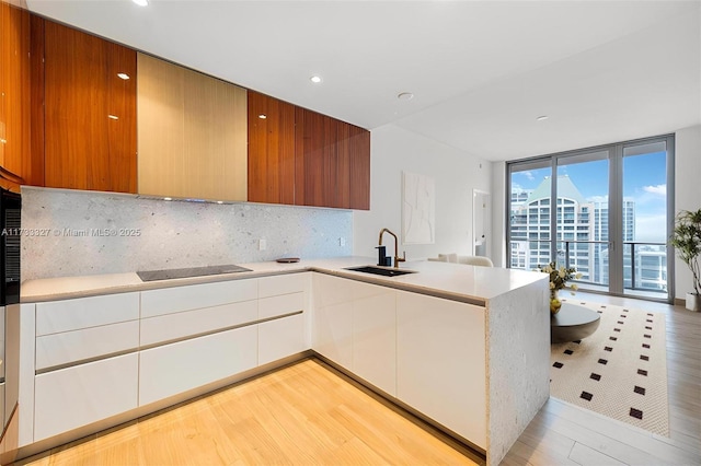 kitchen with white cabinetry, sink, decorative backsplash, expansive windows, and black electric stovetop