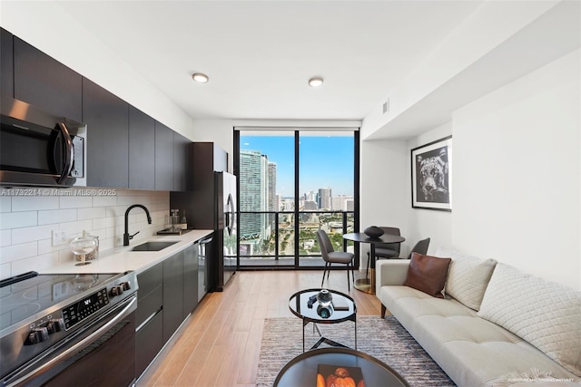 kitchen with sink, light wood-type flooring, appliances with stainless steel finishes, a wall of windows, and backsplash