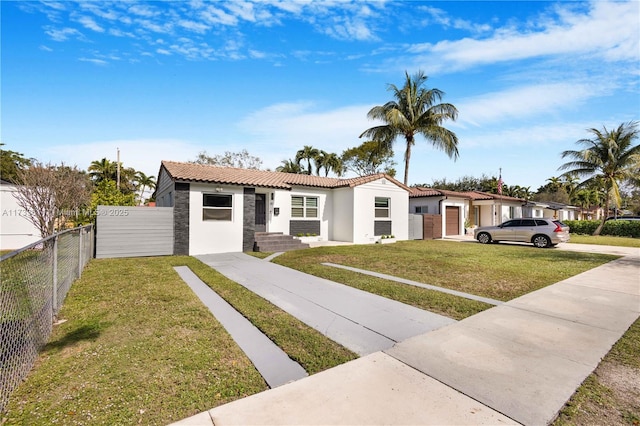 view of front of house featuring stucco siding, stone siding, a tiled roof, fence private yard, and a front yard