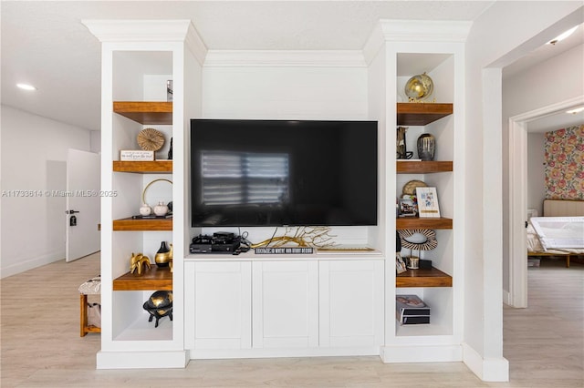 living room featuring built in features, crown molding, light wood-style flooring, and baseboards