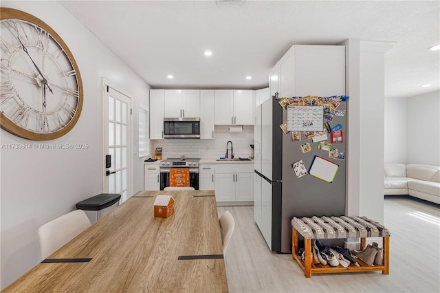 kitchen with stainless steel appliances, a sink, white cabinetry, light countertops, and tasteful backsplash