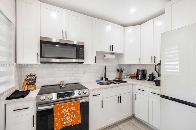 kitchen with stainless steel appliances, tasteful backsplash, light countertops, white cabinetry, and a sink