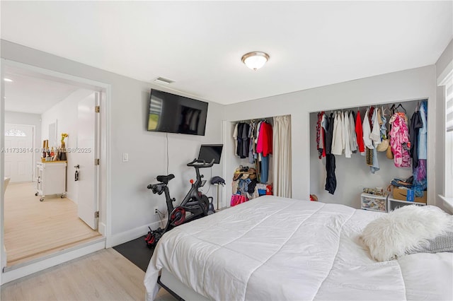 bedroom with multiple closets, visible vents, baseboards, and wood finished floors