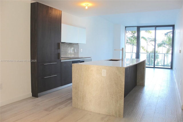 kitchen featuring sink, tasteful backsplash, a center island with sink, light hardwood / wood-style floors, and white cabinets