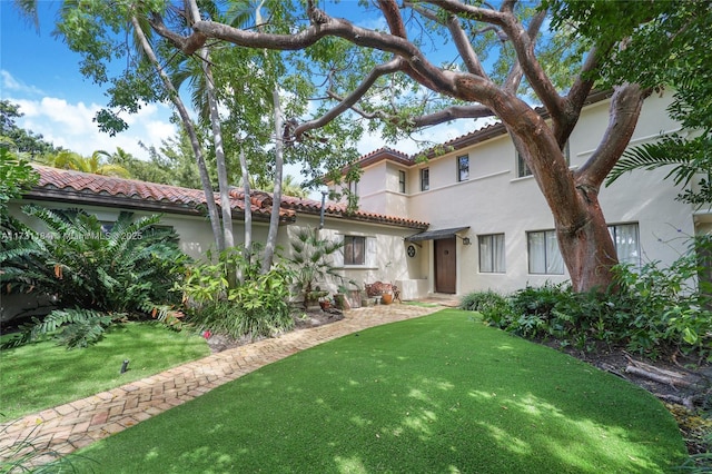 mediterranean / spanish house featuring a tiled roof, a front lawn, and stucco siding