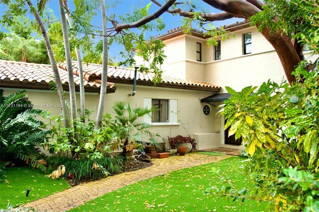 back of property featuring a yard, a tiled roof, and stucco siding