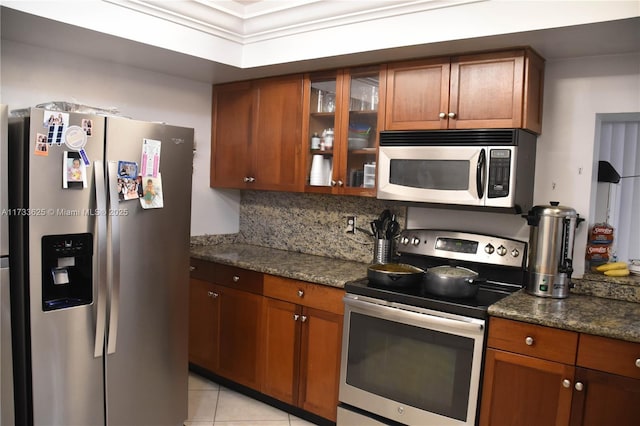 kitchen with tasteful backsplash, stainless steel appliances, light tile patterned flooring, and dark stone countertops