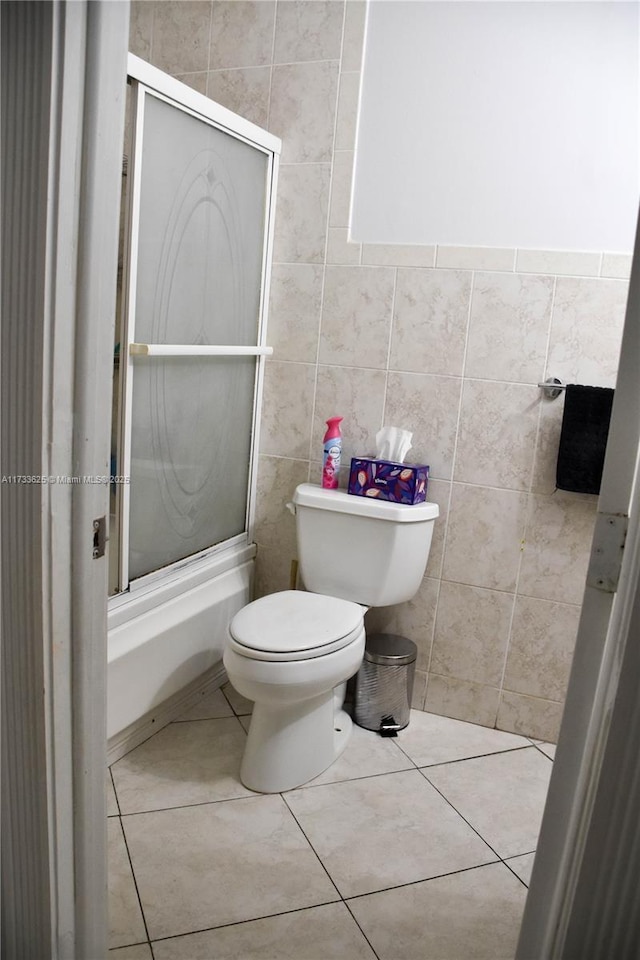 bathroom featuring tile patterned floors, toilet, combined bath / shower with glass door, and tile walls