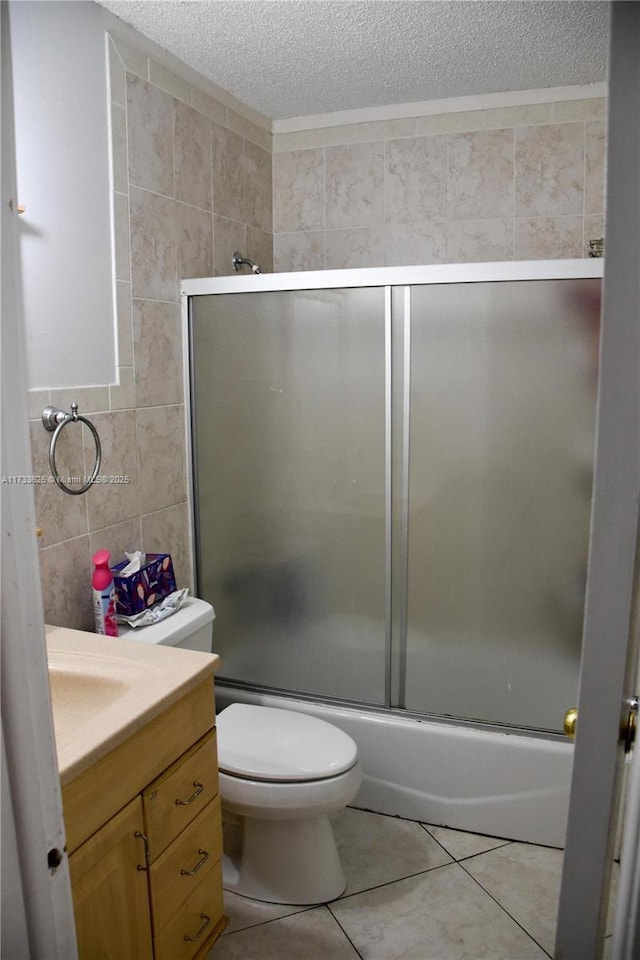 full bathroom featuring tile walls, shower / bath combination with glass door, tile patterned flooring, vanity, and toilet