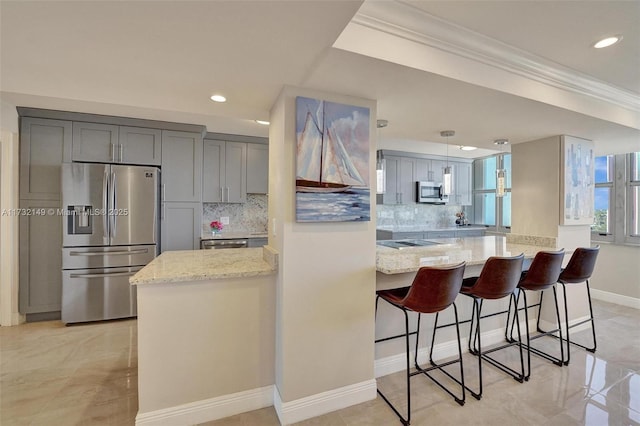 kitchen with a peninsula, hanging light fixtures, appliances with stainless steel finishes, gray cabinets, and light stone countertops