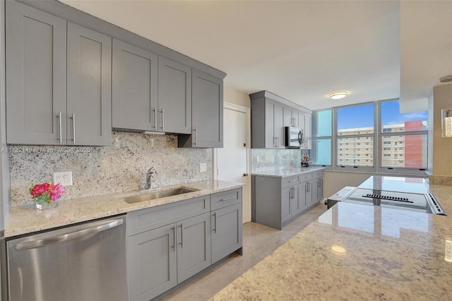 kitchen featuring appliances with stainless steel finishes, gray cabinets, a sink, and light stone counters