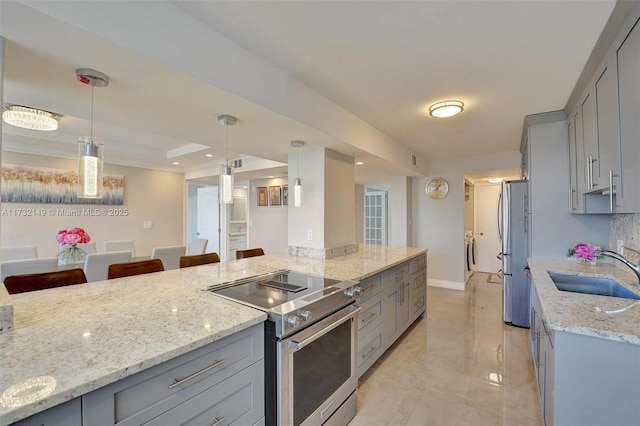 kitchen with appliances with stainless steel finishes, pendant lighting, a sink, and light stone countertops