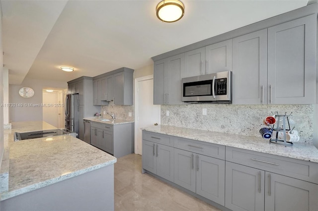 kitchen featuring stainless steel appliances, gray cabinets, a sink, and decorative backsplash