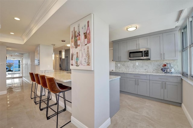 kitchen featuring pendant lighting, a breakfast bar area, stainless steel appliances, gray cabinetry, and light stone countertops