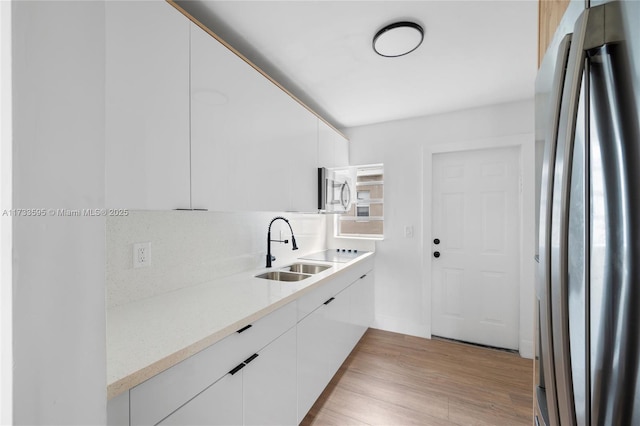 kitchen with tasteful backsplash, white cabinetry, sink, stainless steel appliances, and light wood-type flooring