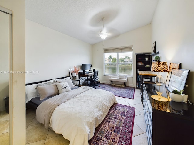 bedroom with light tile patterned flooring, lofted ceiling, ceiling fan, and a textured ceiling