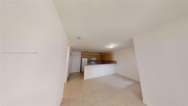 interior space with white appliances, kitchen peninsula, and light tile patterned flooring