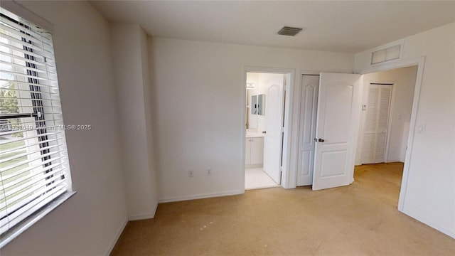 unfurnished bedroom with ensuite bathroom, light colored carpet, and a closet