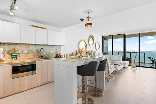 kitchen featuring sink, backsplash, a wall of windows, wall oven, and a water view