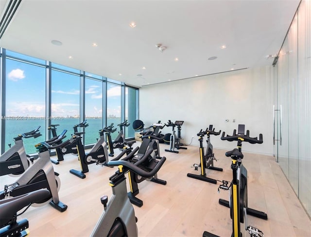 exercise room with a water view, floor to ceiling windows, and light hardwood / wood-style floors